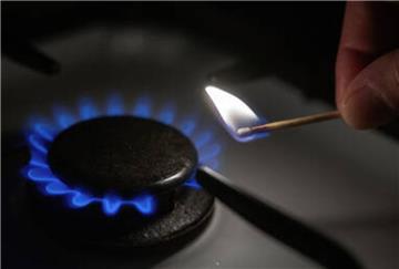 Eine Hand zündet mit einem Streichholz eine Gasflamme auf einem Herd an.