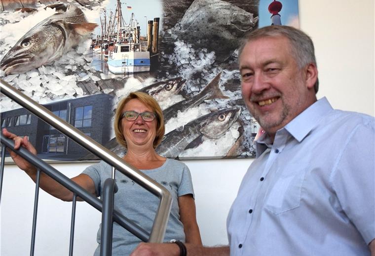 Eiswerk bekommt neuen Chef Ein Mann und eine Frau stehen auf einer Treppe. Im Hintergrund hängt ein Bild, auf dem Fische und Eis gemalt sind.