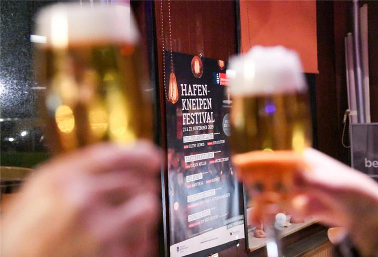 Ein volles Bierglas wird vor einem Plakat in die Höhe gehalten.