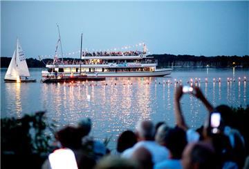 Zahlreiche Besucher verfolgen während der Lichternacht rund 100 Schwimmerinnen und Schwimmer der DLRG, die mit brennenden Fackeln im Wasser schwimmen. Im Rahmen der Lichternacht hat sich der Kurpark in Bad Zwischenahn in ein Farbenmeer verwandelt.
