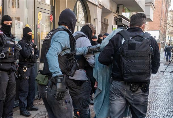 Ein Mann wird bei einer Razzia, mit einer Decke über dem Kopf, von der Polizei abgeführt.