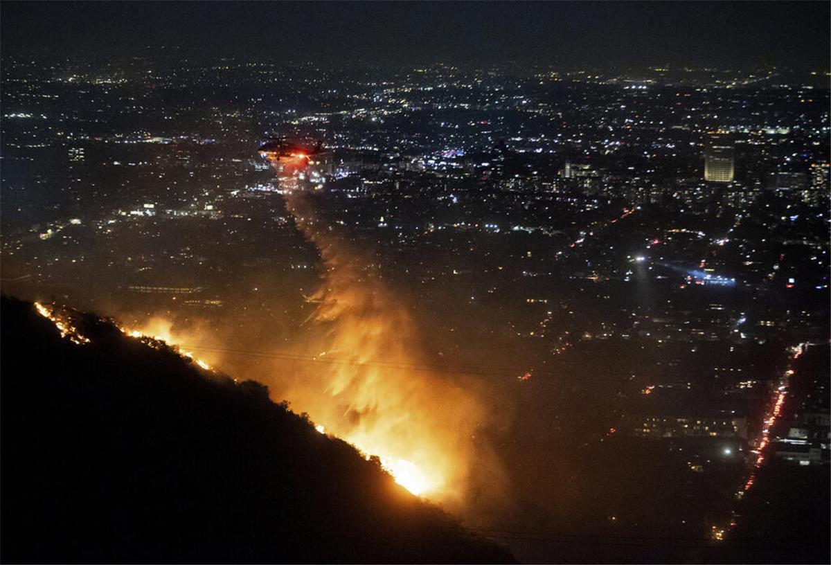 Flammen bedrohen Hollywood: Großfeuer „Sunset Fire“ breitet sich aus 08.01.2025, USA, Los Angeles: Ein Hubschrauber wirft Wasser auf das brennende Sunset Fire in den Hollywood Hills. Foto: Ethan Swope/AP/dpa +++ dpa-Bildfunk +++