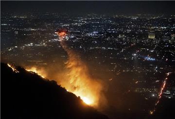 08.01.2025, USA, Los Angeles: Ein Hubschrauber wirft Wasser auf das brennende Sunset Fire in den Hollywood Hills. Foto: Ethan Swope/AP/dpa +++ dpa-Bildfunk +++