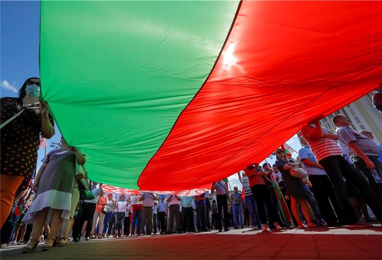 Hunderte Anhänger von Präsident Lukaschenko versammeln sich zu einer Kundgebung auf dem Unabhängigkeitsplatz in Minsk und halten eine riesige Nationalflagge.
