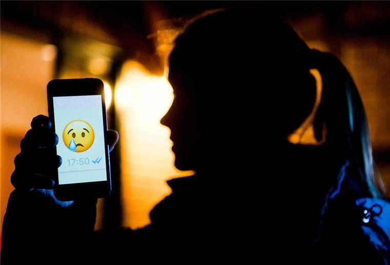 Ein Mädchen hält ein Handy in der Hand. Darauf ist ein trauriger Smiley zu sehen.