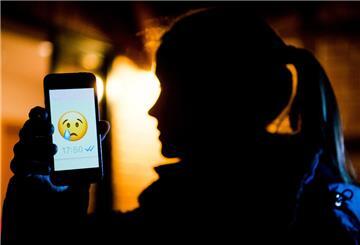 Ein Mädchen hält ein Handy in der Hand. Darauf ist ein trauriger Smiley zu sehen.