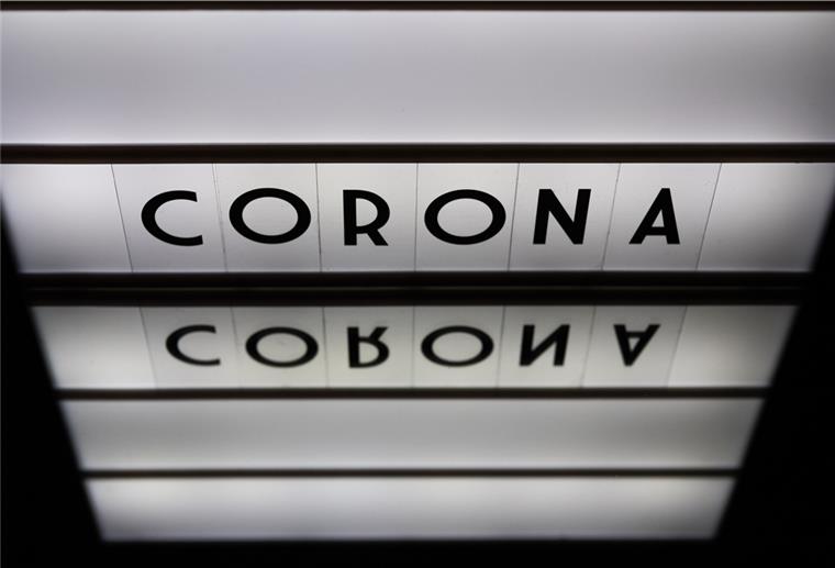 Ein Leuchtkasten mit den Worten Corona, Covid-19, 2020 spiegelt sich in einem Spiegel. (gestellte Szene
