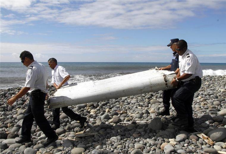 Rätsel um Flug MH370: Im Indischen Ozean startet eine neue Suche Techniker tragen ein Wrackteil, die Flügelklappe eines Flugzeugs, über einen Strand bei Saint-Andre de la Reunion.