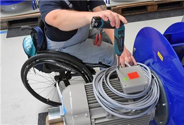 An einem Arbeitsplatz für Motorklemmen ist ein Mitarbeiter im Rollstuhl mit Montagearbeiten beschäftigt.