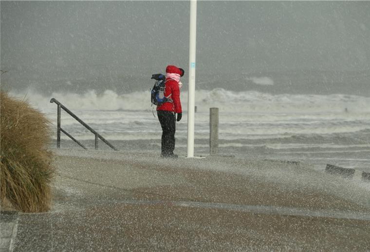 Eine Spaziergängerin blickt auf Norderney auf den Nordstrand und die Wellen der vom Sturm aufgepeitschten Nordsee