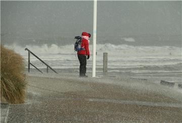 Eine Spaziergängerin blickt auf Norderney auf den Nordstrand und die Wellen der vom Sturm aufgepeitschten Nordsee