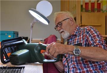 Ein älterer Mann schaut sich ein Werkzeug unter einer Schreibtischlampe an.