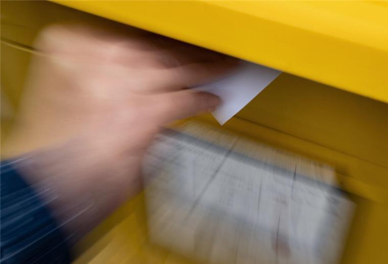 Eine Frau wirft einen Standardbrief in einen Briefkasten