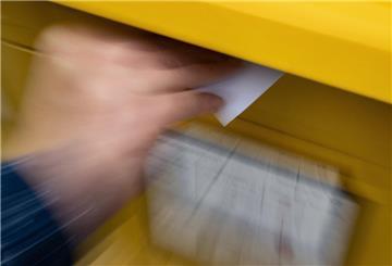 Eine Frau wirft einen Standardbrief in einen Briefkasten