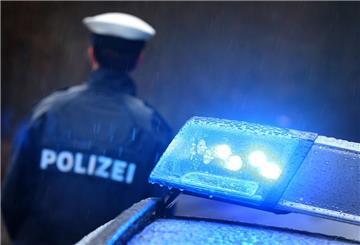  Ein Polizist steht im Regen vor einem Streifenwagen dessen Blaulicht aktiviert ist. 