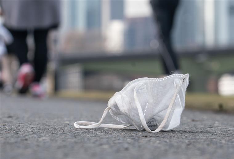 Eine verlorene FFP-2-Maske liegt am Nachmittag am Frankfurter Mainufer zwischen den Spaziergängern und Joggern vor der Kulisse der Hochhäuser. 