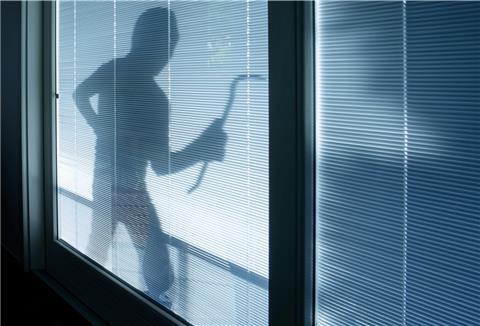 Ein Einbrecher läuft mit Werkzeug vor einem Fenster entlang. 