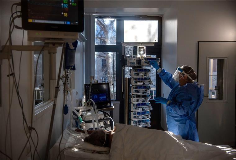 Eine Krankenschwester in Schutzkleidung kümmert sich um einen beatmeten Patienten auf der Intensivstation