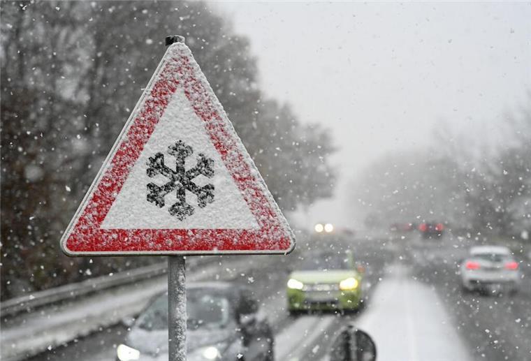Ein Verkehrsschild warnt vor Gefahr von Schnee- oder Eisglätte auf der Fahrbahn, während Schnee fällt. (zu dpa: «Warmfront sorgt für brisante Wetterlage in Niedersachsen»)