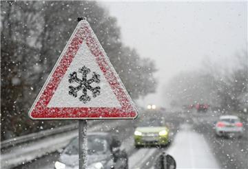 Ein Verkehrsschild warnt vor Gefahr von Schnee- oder Eisglätte auf der Fahrbahn, während Schnee fällt. (zu dpa: «Warmfront sorgt für brisante Wetterlage in Niedersachsen»)