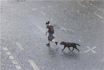 Eine Frau rennt mit ihrem Hund bei Starkregen über eine überflutete Straße.