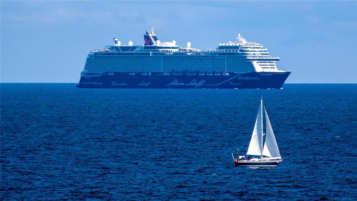 Ein Boot treibt auf dem Ozean, im Hintergrund ein Kreuzfahrtschiff.
