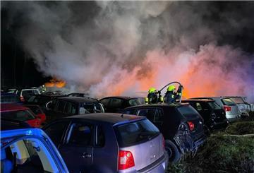 Feuerwehr löschen einen Brand auf einem Gelände mit zahlreichen Autos.