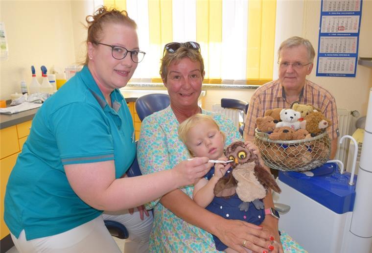 Erwachsene und ein Kind sitzen mit Stofftieren rund um einen Zahnarztstuhl.