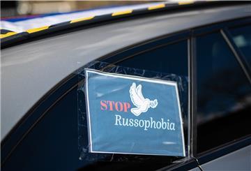 «"Stop Russophobia"» steht auf Plakaten geschrieben, das bei einem Autokorso an einem Auto angebracht ist. 