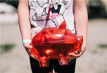 Ein Kind hält eine rotes Sparschwein vor dem Körper. In Deutschland muss der Antrag für das Kindergeld noch aktiv gestellt werden. Wir klären die wichtigsten Fragen, die Eltern haben.