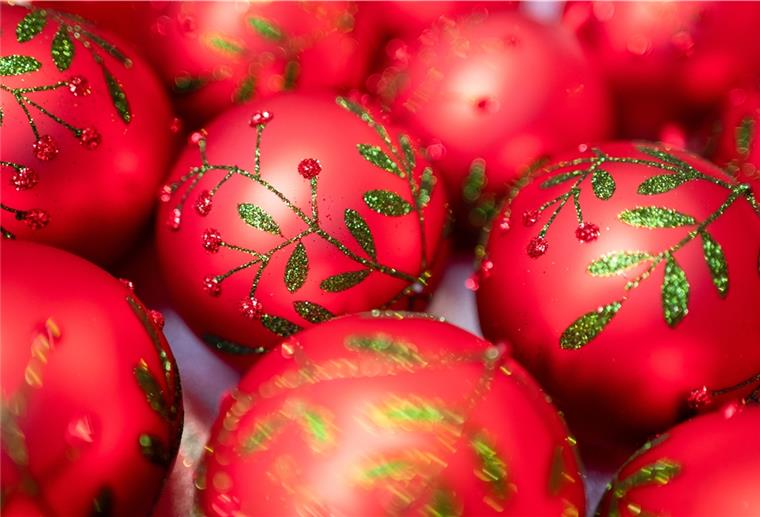 Im harten Lockdown: So darfst du Weihnachten feiern Roter Christbaumschmuck mit grünem Glitzer liegt nebeneinander auf dem Tisch.