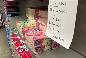 Ein halbleeres Supermarkt-Regal mit einem Hinweisschild, das zu maßvollem Einkaufen von Klopapier und Küchentüchern aufruft. 