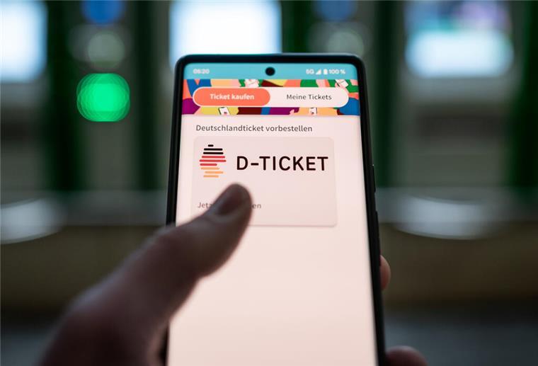 Ein Mann hält ein Mobiltelefon, auf dem das „D-Ticket“ gekauft werden kann, vor Ticketautomaten in der Hand.