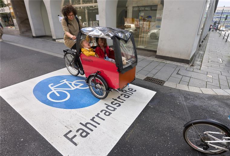 Frau fährt mit einem Lastenrad und zwei Kindern auf einer Fahrradstraße