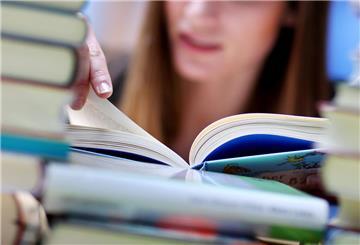 Eine junge Frau liest an einem Tisch voller Bücher.