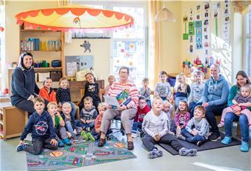Kindergartenkinder sitzen im Halbkreis neben Vorleseomi Erika