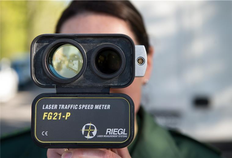 Eine Polizeihauptmeisterin schaut im Rahmen einer Geschwindigkeitsmessung durch ein Lasergerät. 