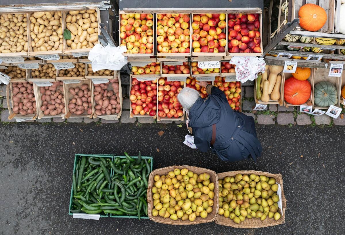 Eine Frau steht auf einem Wochenmarkt an einem Stand mit Obst und Gemüse. 