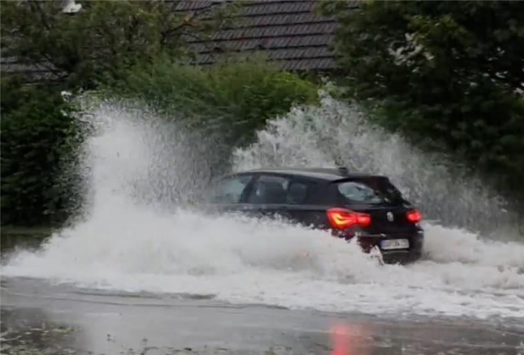 Wieder Unwetter in Teilen Deutschlands Ein Auto fährt durch das stehende Wasser auf einer Straße im Ort und schiebt eine Bugwelle vor sich her.