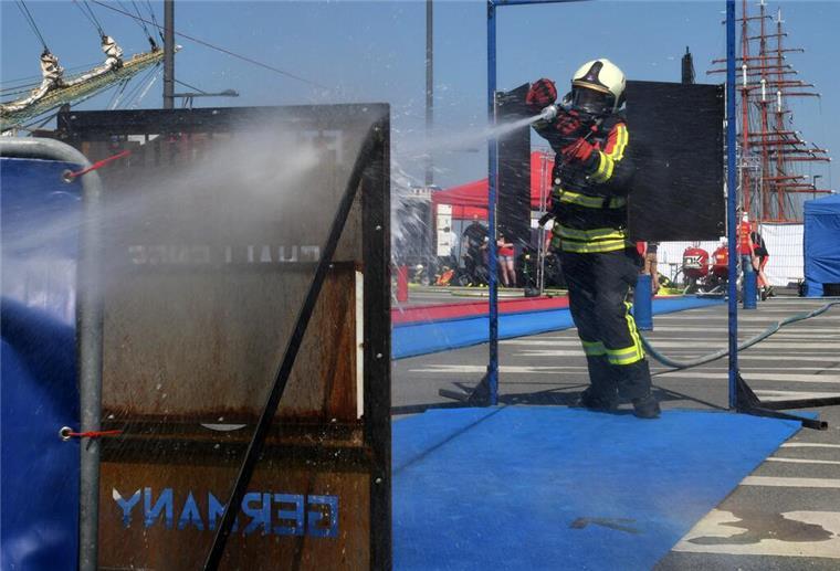 Ein Feuerwehrmann in Schutzausrüstung spritzt während eines Wettbewerbs mit seinem Löschschlauch auf ein Ziel. 