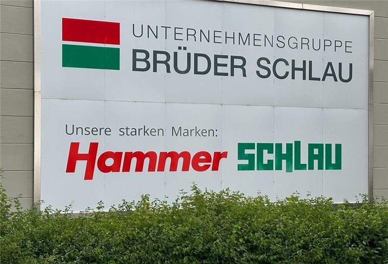 Das Logo der Unternehmensgruppe Brüder Schlau GmbH & Co KG und das des Raumaustatters Hammer ist auf einem Schild zu sehen.