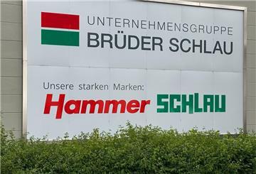Das Logo der Unternehmensgruppe Brüder Schlau GmbH & Co KG und das des Raumaustatters Hammer ist auf einem Schild zu sehen.