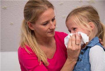 Eine Frau putzt einem Kind die Nase. Wenn das Kind krank ist, gibt es oft Anspruch auf Kinderkrankengeld.