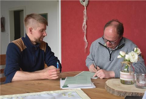 Das Foto zeigt den frischgebackenen Biobauern Jan Kaiser bei der Vertragsunterzeichnung. Daniel Bischoff, Erzeuger- und Umstellungsberater bei Bioland, schaut ihn dabei zu.  