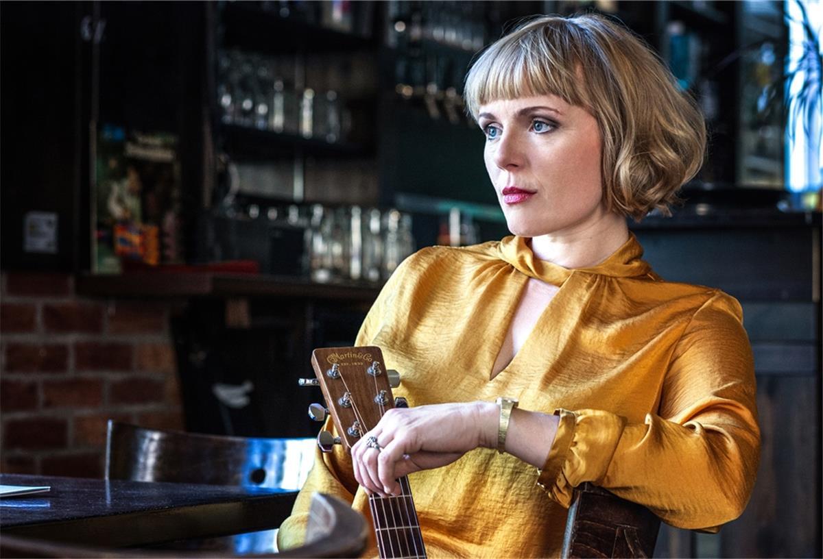 Shey singt und spielt Soul im Pferdestall Frau mit Gitarre an einem Kneipentisch.