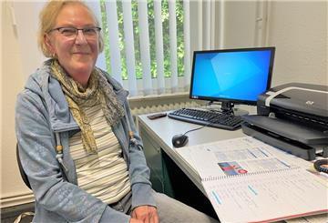 Karin Herrmann sitzt an einem Schreibtisch, auf dem ein Computerbildschirm steht.
