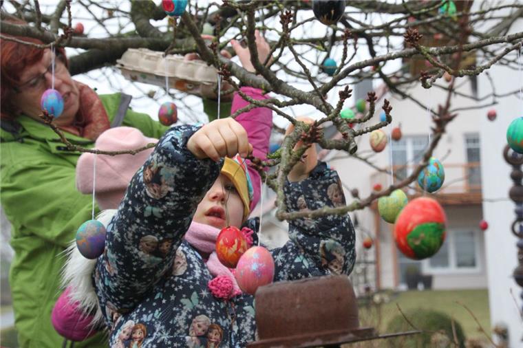 Kinder helfen dabei, die vielen bunten Ostereier in die Japanische Kirsche zu hängen. 