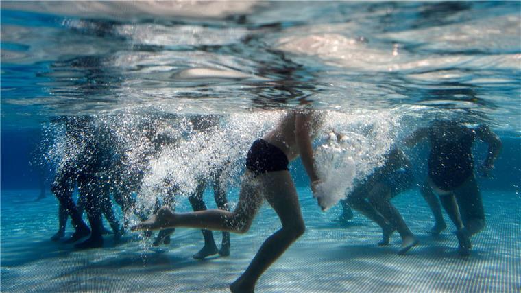 Kinder spielen im Becken eines Freibads.