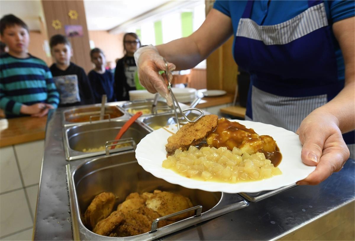 Kita Klein Meckelsen: Mensa jetzt oder später? Das Foto zeigt ein Frau, wie sie in der Mensa Fleisch und Gemüse auf einen Teller tut.