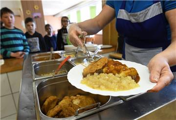 Das Foto zeigt ein Frau, wie sie in der Mensa Fleisch und Gemüse auf einen Teller tut. 